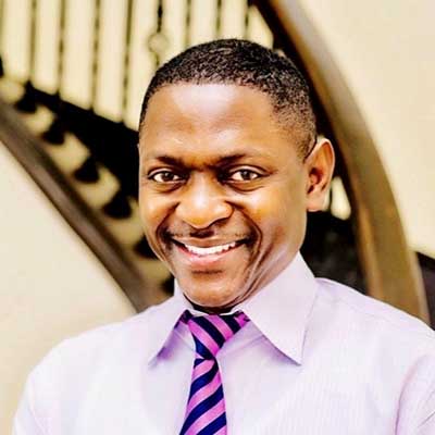 Portrait of a black man smiling wearing a light purple dress shirt and purple and black striped tie.