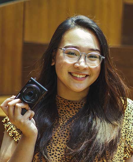 Portrait of an asian woman smiling holding a camera with her right hand.