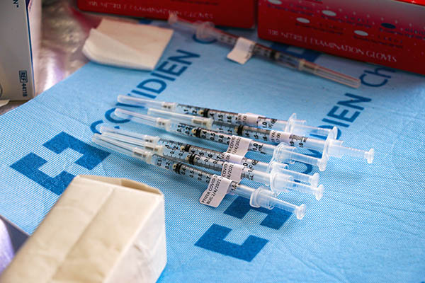 A pile of syringes filled with vaccines on a light blue pad.