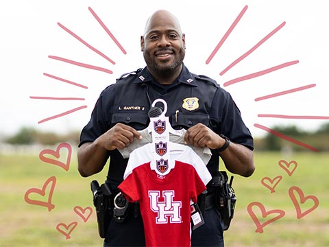 Photo of Sergeant Leonard Ganther in police uniform holding a set of UH branded baby outfits.