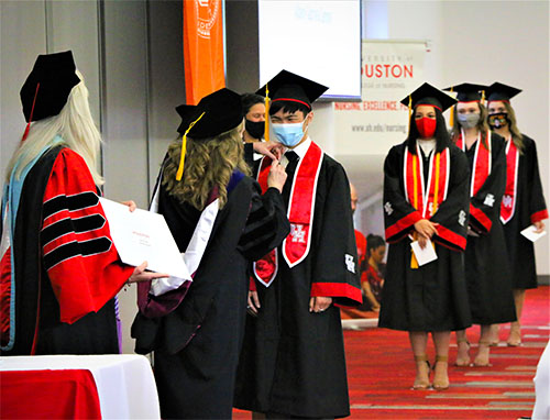 Two Nursing faculty stand in front of a line of students wearing face masks. One faculty attaches a pin to the first student's shirt.