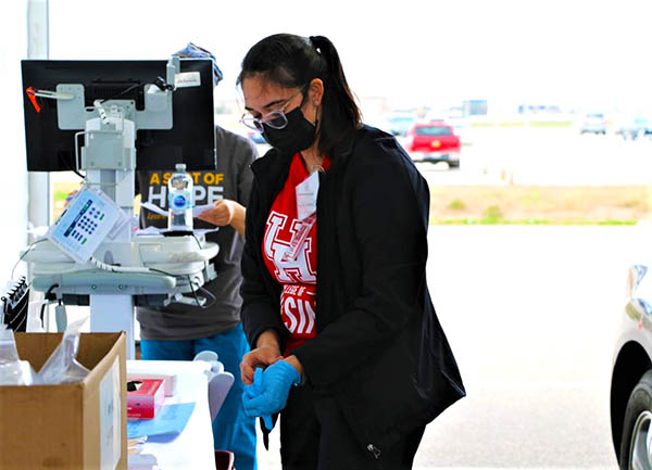 A nurse in a red shirt puts on a glove while in front of a computer station