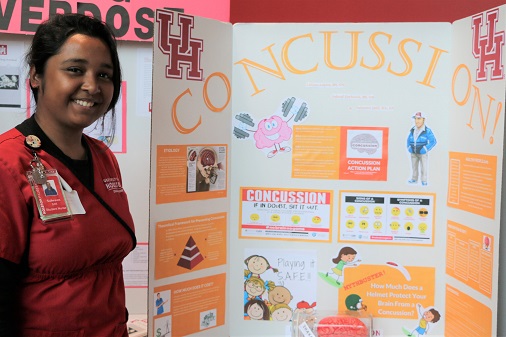 A female nursing student stands next to a research poster about concussions