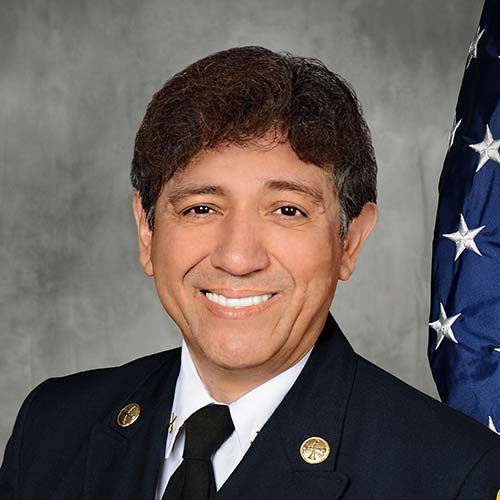 Portrait of a Hispanic man smiling with short curly hair wearing a navy blue business suit