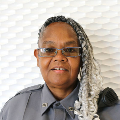 Portrait of a black woman with braided gray and white hair wearing glasses and a grey button-up shirt