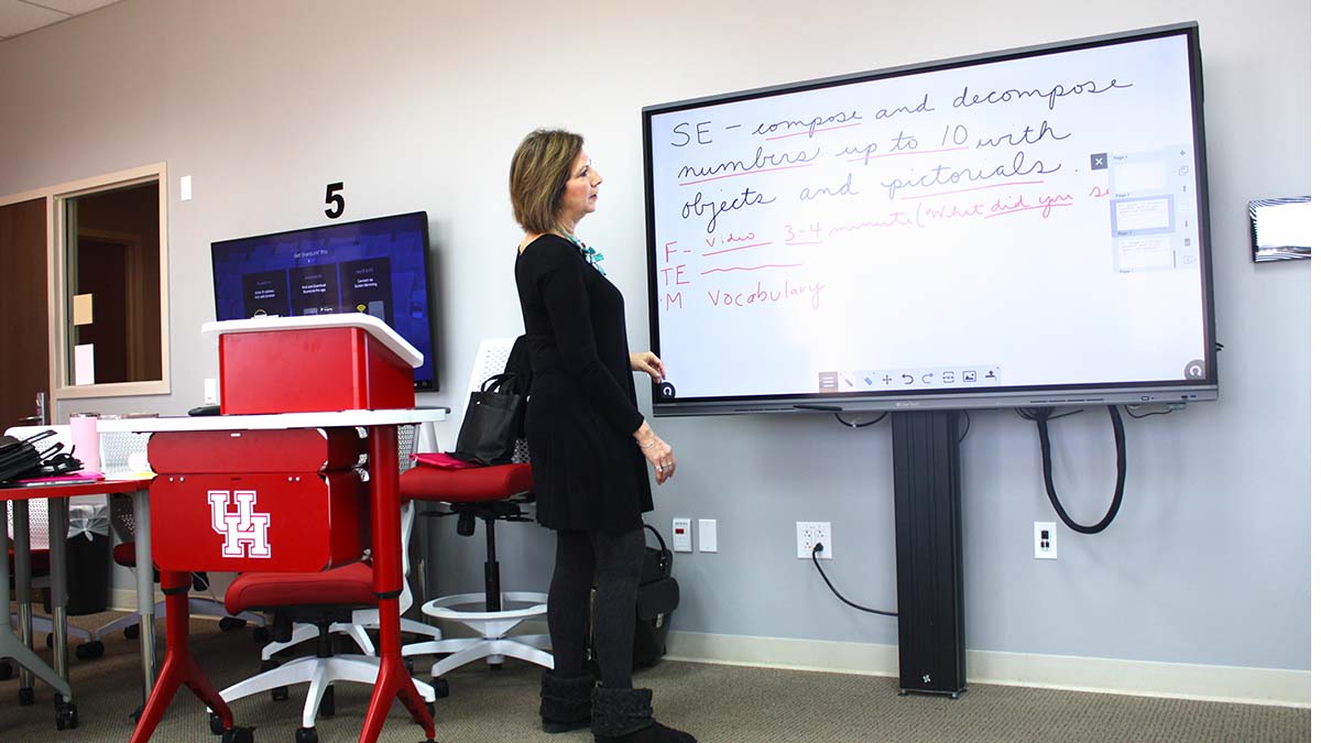 A woman stands in front of an interactive monitor on which she has used her finger to hand write notes.