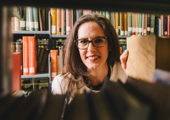 Image of Christina Gola smiling in between bookshelves.