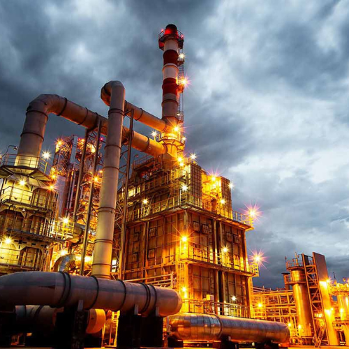 An expansive oil refinery with numerous pipes and bright lights, showcasing industrial activity at dusk.