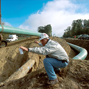The easy way: a worker directs a sideboom operator to lay a new 42-inch piece of pipe into a trench with an existing 26-inch white pipe to carry natural gas. Photo by Robert Nickelsberg/Liaison Getty Images